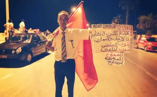 At a protest the evening following a mass beach shooting attack, a Tunisian man in Sousse holds up a banner in French and Arabic condemning ISIL and showing solidarity with the foreign tourists who were targeted. Image by Alice Su. Tunisia, 2015. At a protest the evening following a mass beach shooting attack, a Tunisian man in Sousse holds up a banner in French and Arabic condemning ISIL and showing solidarity with the foreign tourists who were targeted. Image by Alice Su. Tunisia, 2015.