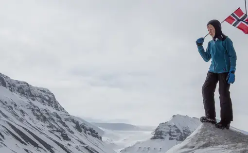 A child carries a Norwegian flag on a high Arctic landscape. Image by Amy Martin. Norway, 2018.