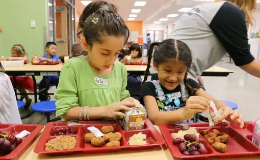 The food at school is unfamiliar. Hala just pokes at her "wiener dogs." She struggles to open a milk carton while the girl beside her wrestles with a ketchup packet