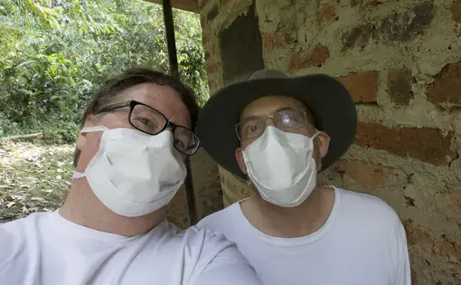Milwaukee Journal Sentinel photojournalist Mark Hoffman (left) and reporter Mark Johnson are shown inside Kibale National Park in Uganda. They are wearing masks while photographing and examining large bats, which are renowned for their ability to carry pathogens. Kibale Forest boasts the highest number of primate species in the world. Image by Mark Hoffman. Uganda, 2017. Milwaukee Journal Sentinel photojournalist Mark Hoffman (left) and reporter Mark Johnson are shown inside Kibale National Park in Uganda. They are wearing masks while photographing and examining large bats, which are renowned for their ability to carry pathogens. Kibale Forest boasts the highest number of primate species in the world. Image by Mark Hoffman. Uganda, 2017.
