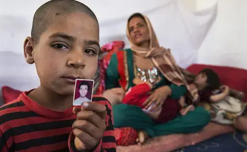 Hamid, in 2014, holds a photo of his father, who was killed during his service in the Afghan army, leaving Fereshta, at rear, widowed with five children. Image by Paula Bronstein/The Wall Street Journal. Afghanistan, 2014. Media file: bn-kk496_0915af_p_20150921183833.jpg