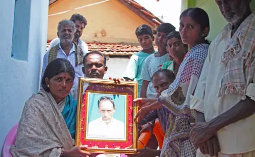 Gopamma Nayaka, surrounded by family and neighbors, holds the portrait of her husband Hanamuantha, who was killed and eaten by a tiger in India's Bandipur National Park and Tiger Reserve. Image by Rachel Nuwer. India, 2019.