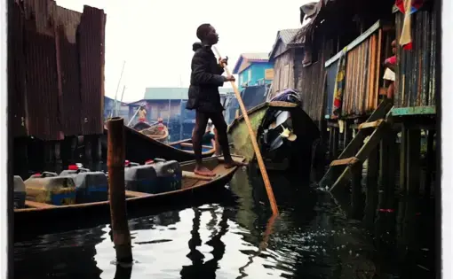 From the Everyday African Instagram feed (@everydayafrica): "A man visits from his boat in Iwaya—a neighborhood partially on stilts in the black waters of the Lagos Lagoon—in Lagos, Nigeria, August 16, 2013." Image by Allison Shelley. Nigeria, 2013.