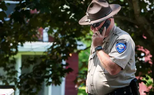 A deputy with the Lincoln County Sheriff's Office takes a phone call outside the scene of an investigation in Boothbay Harbor in this 2015 file photo. Image by Ashley L. Conti/BDN. United States, 2015.