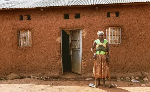 A Rwandan woman stands in front of her home. Image by sifkigali/Shutterstock. Rwanda, 2015.