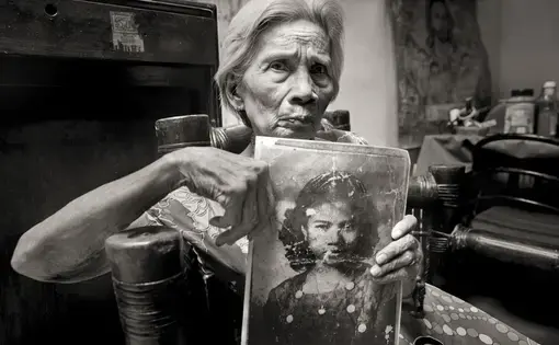 Fedencia Nacar David holds her photo for an application to work as a maid. She was 15. A year before, a Japanese soldier sliced her ear and threatened to behead her if she didn't go to a garrison with him; she was raped over 10 days. "It still hurts," she says. "I was innocent. Why did that happen to me?" She kept her past from her children until "comfort women" began speaking out in the 1990s. Image by Cheryl Diaz Meyer. Philippines, 2019.