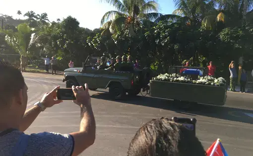 The remains of Fidel Castro traveled along a 500 mile journey from Havana to Santiago, his final resting place—the exact reverse journey Castro took when he launched his 1959 revolution. Image by Zach Fannin. Cuba, 2016. Fidel Castro's remains are transported 500 miles from Havana to Santiago. The image shows an open car pulling a trailer holding his remains, surrounded by flowers.
