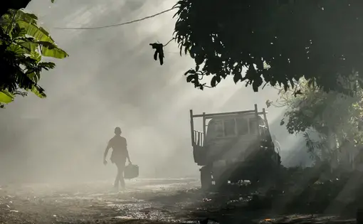 A man walks through clouds of smoke from burning rubbish in the village of Ouani, Anjouan, a popular departure point for Comorian migrants leaving for Mayotte. Image by Tommy Trenchard. Comoros, 2019.