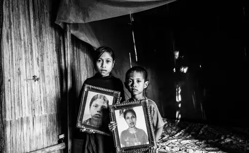 Dolfina’s children Erna and Julius hold photos of their mother inside their hut in East Nusa Tenggara, Indonesia. They now live with their grandfather Mikhael. Image by Xyza Bacani. Indonesia, 2018.