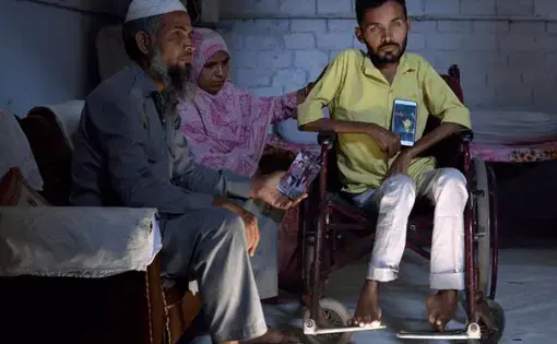 Umar Khan, 24, with his parents shows photos of his younger brother Azhar who died last year. Azhar was suffering from muscular dystrophy as is Umar. Umar watched his younger brother dying just last year and he knows that is coming to him in a few short years. Umar’s parents are very caring towards him. They feed him, wash him and help him in the toilet. He needs 24 hour care. That’s what they were doing for both children until last year. Image by Rohit Jain. India, 2019.