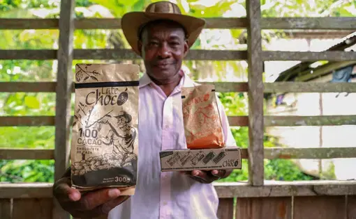 José Palacios, a cacao farmer, holds the Late Chocó chocolate products produced by his son, Joel, in Bogotá. The package bears an illustration of his likeness. José Palacios lives in Colombia's western Chocó department, which is also a coca-growing region. Image by Verónica Zaragovia. Colombia, 2018.