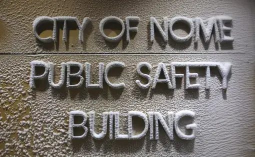 In this Feb. 21, 2019, photo, a snow-encrusted sign marks the entrance to the police station located on a tundra road on the outskirts of Nome, Alaska. An internal cold case audit launched in 2019 has uncovered evidence that the agency regularly failed to fully investigate sexual assaults. Image by Wong Maye-E. United States, 2019.