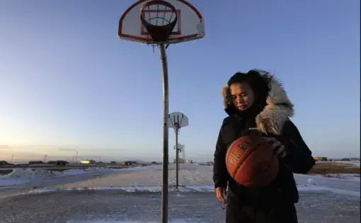 In this Feb. 17, 2019, photo, Deidre Levi carries her basketball as she walks to work in the Native Village of St. Michael, Alaska. Levi says she spoke up about being sexually assaulted because she wanted to be a role model for girls in Alaska. Image by Wong Maye-E/Associated Press. United States, 2019.