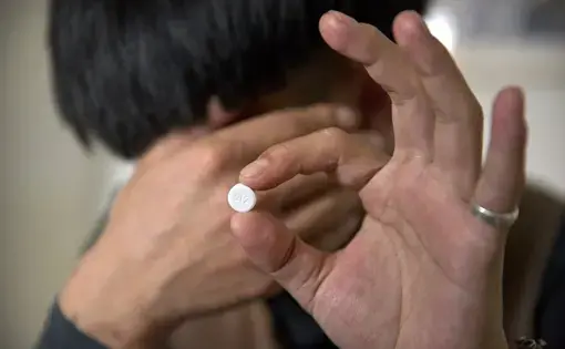 In this March 28, 2019, photo, Yin Hao, who also goes by Yin Qiang, holds a Tylox pill while sitting in a tea house in Xi'an, northwestern China's Shaanxi Province. Officially, pain pill abuse is an American problem, not a Chinese one. But people in China have fallen into opioid abuse the same way many Americans did, through a doctor's prescription. And despite China's strict regulations, online trafficking networks, which facilitated the spread of opioids in the U.S., also exist in China. Image by Mark…