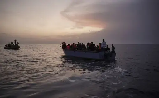 In this Sept. 19, 2019 photo, migrants on an overcrowded wooden boat wait to be rescued by the Ocean Viking humanitarian ship in the Mediterranean Sea. The misery of migrants in Libya has spawned a thriving and highly lucrative business, in part funded by the EU and enabled by the United Nations, an Associated Press investigation has found. Image by Renata Brito/AP Photo. Libya, 2019.