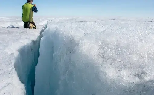 University of Montana glaciologist Joel Harper examines a deep crack in the ice sheet called a crevasse. Image by Amy Martin. Greenland, 2018.