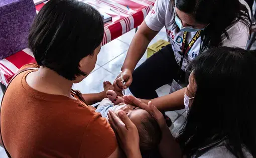 Rosalie Natividad administers a vaccine to a baby in a clinic. Image by Xyza Cruz Bacani. Philippines, 2020.