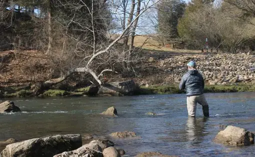 A man stands in a river and casts his fishing line into the water.