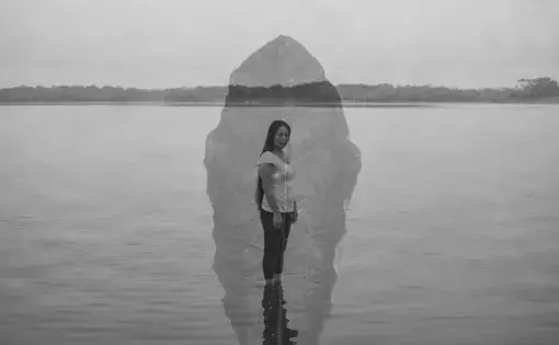 Black and white double exposure photo of a woman standing in front of a body of water with a leaf superimposed on the image.
