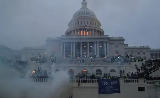 Far-right rioters rush the front steps of the U.S. Capitol building with the dome in the background.