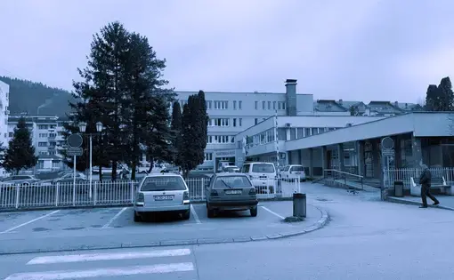 Blue-tinted image of a hospital with parking lot in front.
