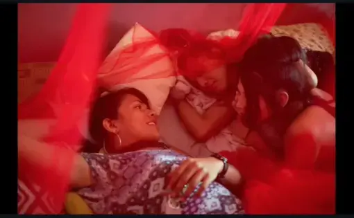 Three transgender women lie on a bed talking in Honduras. They are cloaked in a red mesh canopy.