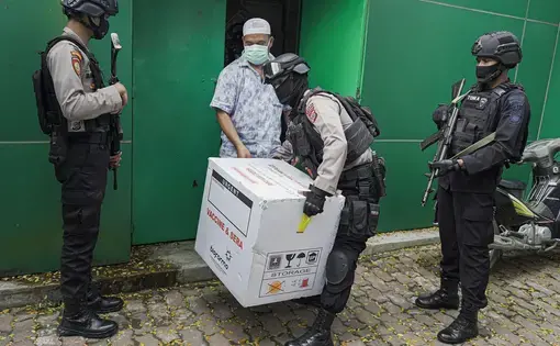 A police officer carries a large box full of vaccines.