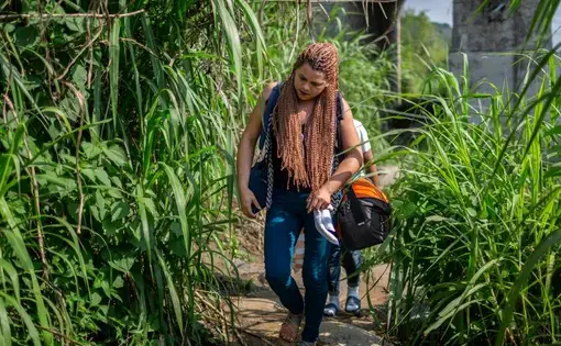 natgeowomenonthemove.jpg A young woman with long braids walks down a stone path with foliage on either side of her. She's wearing jeans and sandals and carries with her a duffel bag and a purse.