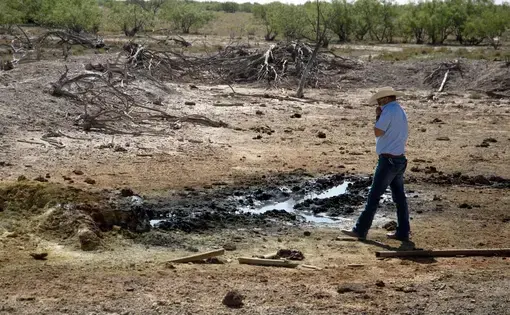 A conservation official holds his shirt over his nose as he approaches an oil-sheened pond created by an abandoned well.