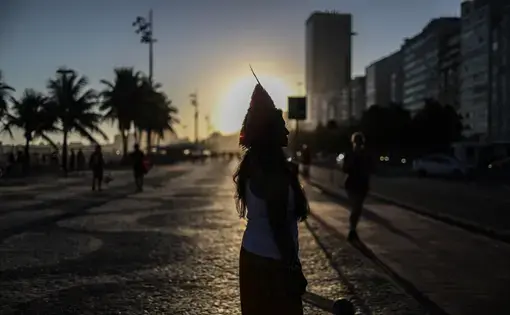 The silhouette of a woman in a headdress standing against the sun as it sets.