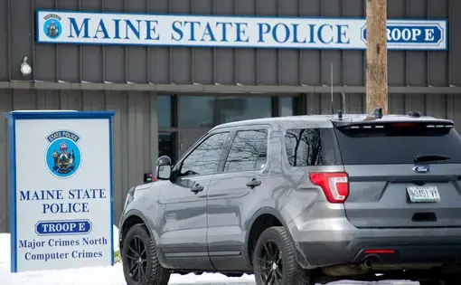 A gray SUV is parked in front of a Maine State Police building.