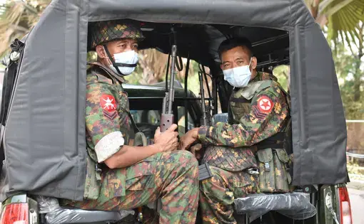 Soldiers in medical face masks sit in a truck.