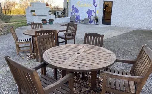 An outdoor space with sets of tables and chairs with potted plants. A mural on a wall reads, "The healing starts here."