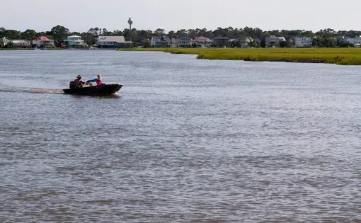 Two people ride a small boat through a lake surrounded by houses.