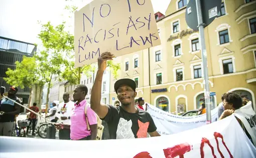 A Nigerian asylum seeker holds up a sign reading "No to racist asylum laws" during a protest