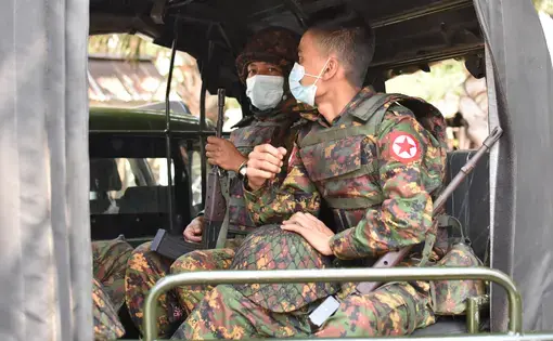 Soldiers wearing medical masks sit in a vehicle.