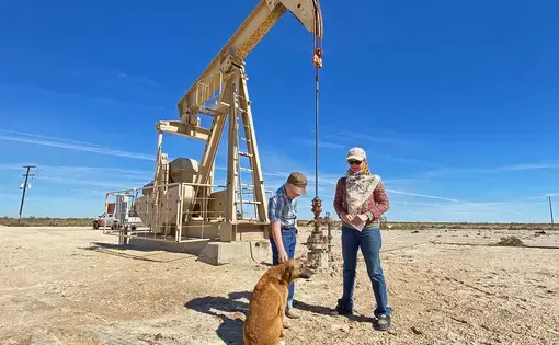 Two people and a dog stand in front of a well with extraction machinery.