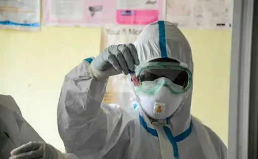 A person in PPE holds up a vial.