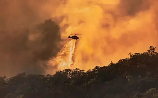 Fire fighting helicopter carrying water bucket to extinguish the forest fire below