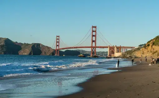 Image of the San Francisco coast with a few beach goers and the golden gate bridge in the distance.