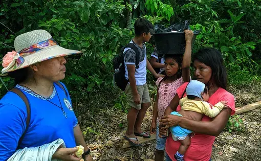 Two people, one carrying a baby, speak to a missionary.
