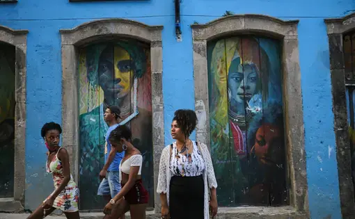 A portrait of Rutian Pataxó in front of a building with murals on it.