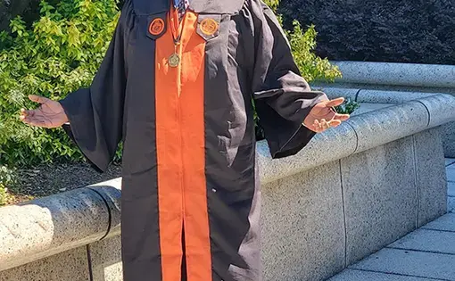 Michael Watkins stands outside in a graduation cap and gown.