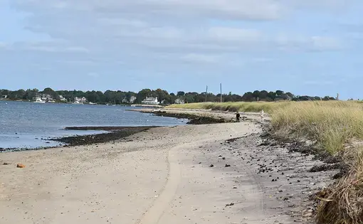 A sandy beach with a man walking alongside the water.