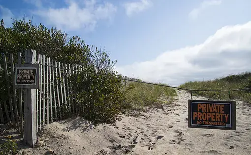 A sandy path to the beach has been cordoned off with two signs that read "Private Property No Trespassing."