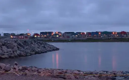 Buildings glow with lights in the distance, behind a body of water.