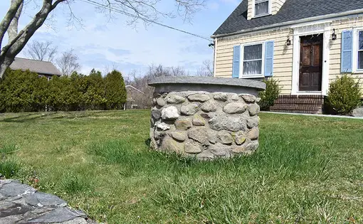 Image shows a stone well in the front yard of a yellow house in Rhode Island.