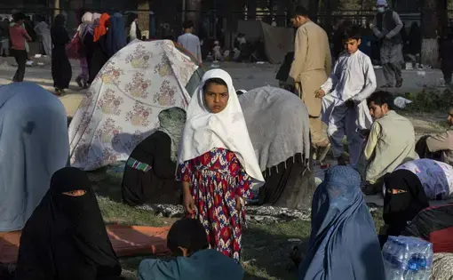 girl stands amongst displaced Afghans