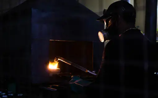 Man in a small refinery melts gold and burns the mercury. He uses a mask to avoid the toxic vapor
