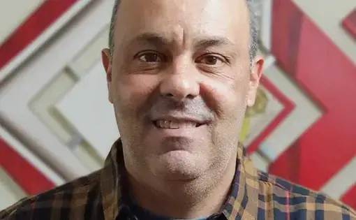 A man wearing a yellow stripe flannel shirt smiles at the camera.